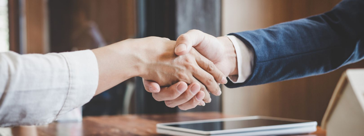 Close up of two people shaking hands over a signed contract and set of keys on a desk.